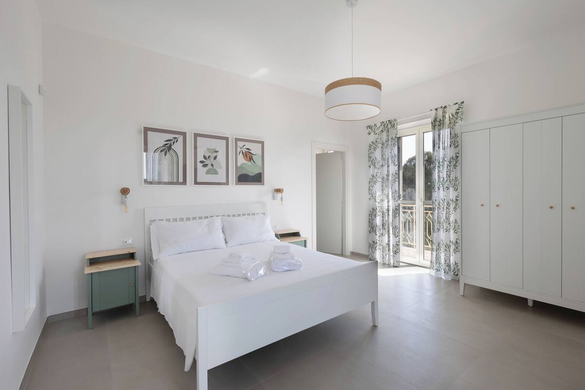 A bedroom with a bed, bedside tables, a wardrobe, and a view of the outdoors.