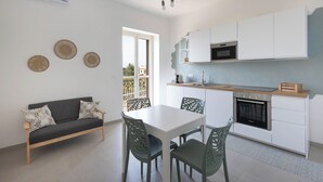 A modern kitchen with white cabinets, a built-in oven, and a dining area with a table and chairs. - PORTA SUGLI ULIVI (Monopoli)