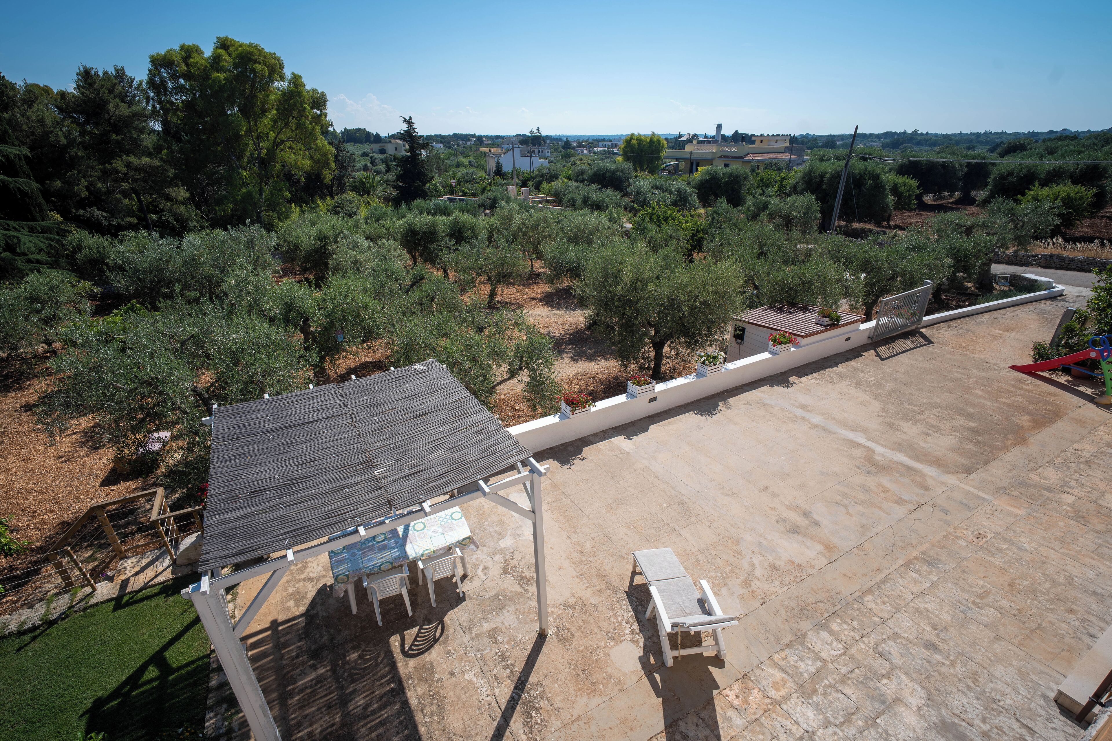 Una terraza en la azotea con una mesa y sillas, rodeada de olivos y vistas al campo.