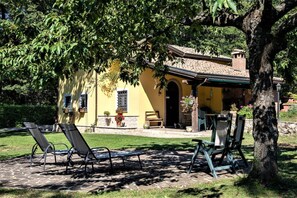 A yellow building with a patio area, outdoor seating, and a tree providing shade.