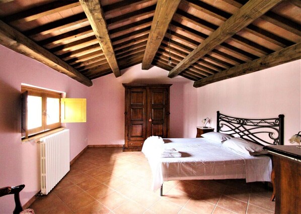 A bedroom with a bed, wooden ceiling beams, a radiator, and a wardrobe.
