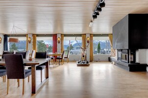 Amplia sala de estar con piso de madera, una mesa de comedor con sillas, una chimenea y un ventanal con cortinas.