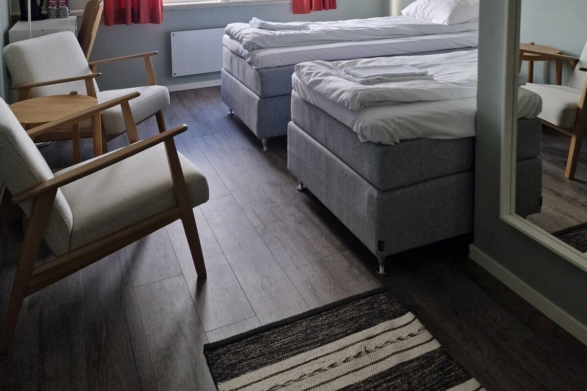 Une chambre avec deux lits, un bureau, des chaises, une fenêtre avec des rideaux et une vue sur les montagnes.