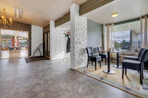 Un amplio espacio interior con suelo de baldosas de piedra, una mesa de comedor con sillas y vistas al exterior a través de grandes ventanales.