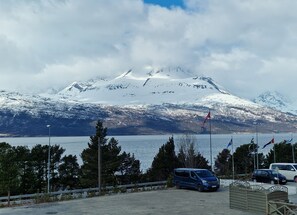 Parkkipaikka, jonka taustalla kohoaa vuori, ja näkymässä on myös vesistö ja lippuja.