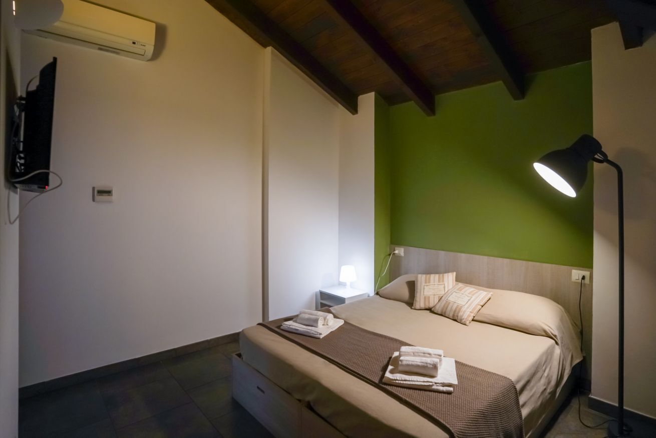 A bedroom with a bed, bedside table, lamp, and a wall-mounted air conditioner.