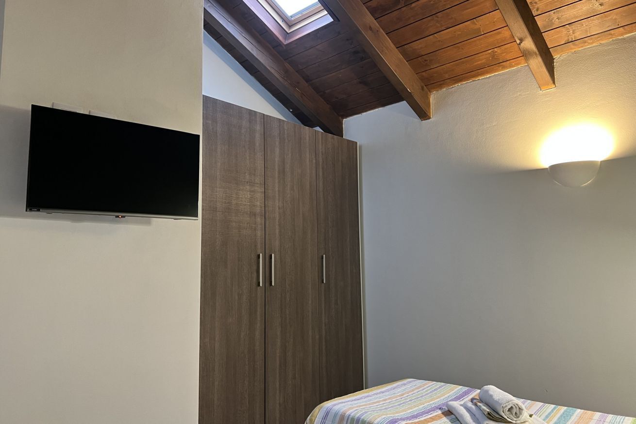 A bedroom with a bed, a wardrobe, a TV, and a skylight.