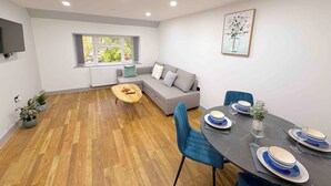 A modern living room with a grey sofa, a wooden coffee table, and a dining area with blue chairs and a black table. - The Modern muse (Birmingham)