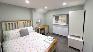 A bedroom with a bed, a bedside table, a mirror, a radiator, and a window. - The Modern muse (Birmingham)