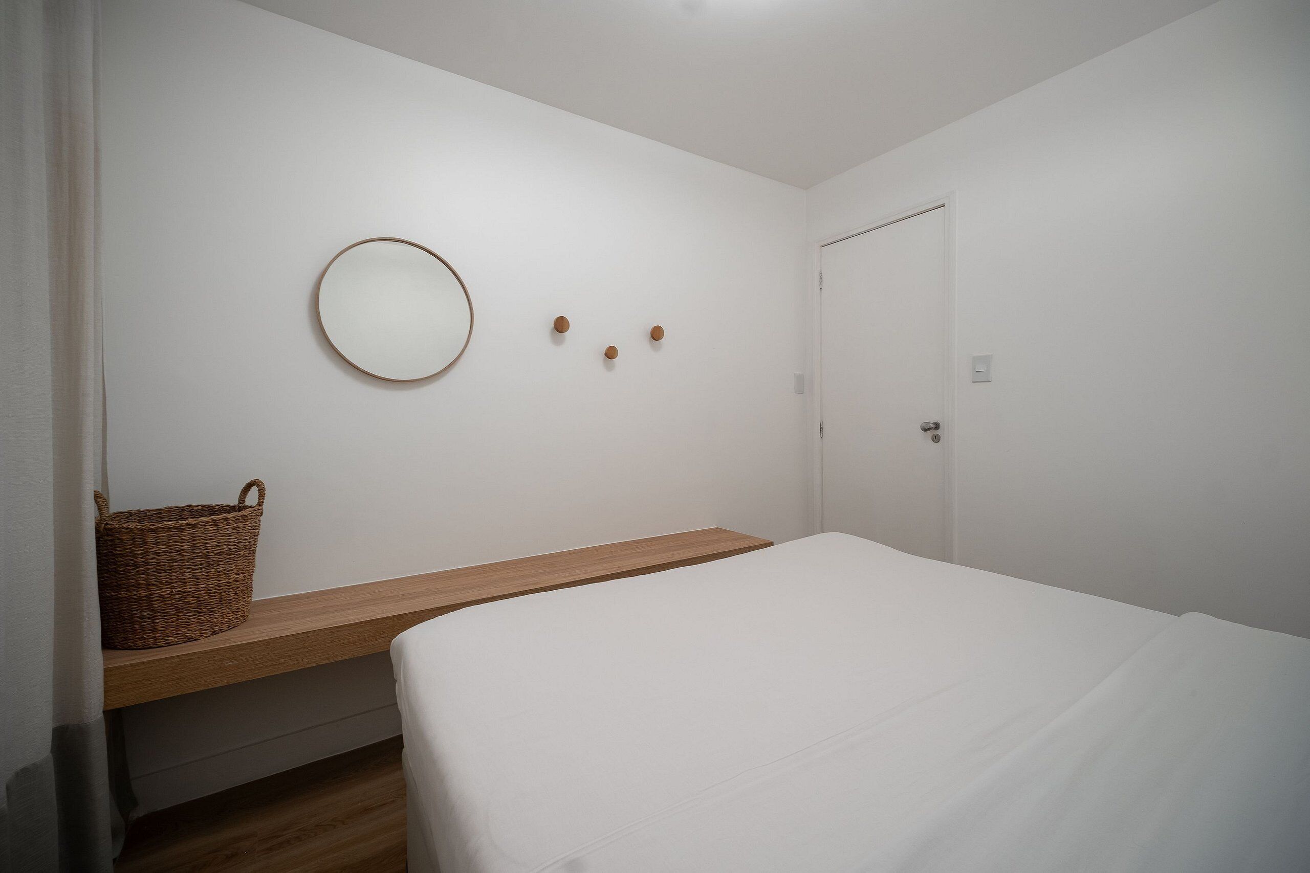 A bedroom with a bed, a wooden bedside table, a round mirror, and a basket.