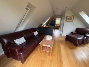 A spacious loft with a high ceiling, a dark brown leather sofa, a matching armchair, and a wooden coffee table. A kitchen area is visible in the background. - Tranquil Pond View Loft Retreat in Sudbury (Sudbury)