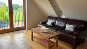 A living room with a brown leather sofa, a wooden coffee table, and a sliding glass door leading to a balcony. - Tranquil Pond View Loft Retreat in Sudbury (Sudbury)