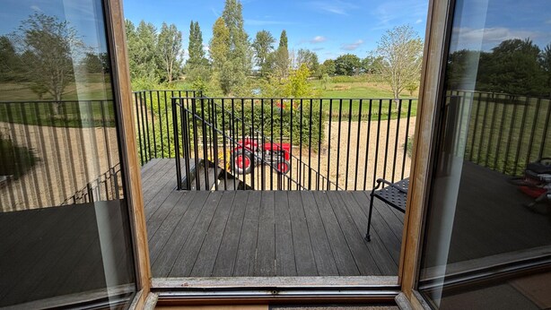 A wooden deck with a black metal railing, a red tractor, and a grassy field with trees in the background. - Tranquil Pond View Loft Retreat in Sudbury (Sudbury)