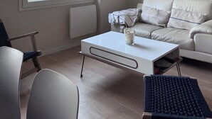 A modern living room with a white sofa, a coffee table, a wicker chandelier, and a large window with autumn foliage view. - RENTAL HOUSE 2 BEDROOMS IN THE CENTER OF PORNIC FOR 4 PEOPLE (Pornic)