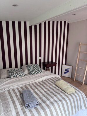 A neatly made bed with striped bedding, a wooden nightstand with a framed picture, and a wooden ladder against the wall. - RENTAL HOUSE 2 BEDROOMS IN THE CENTER OF PORNIC FOR 4 PEOPLE (Pornic)