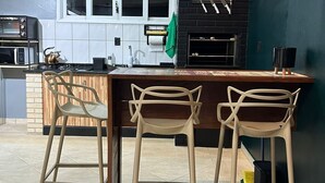A modern kitchen with a central island, bar stools, a microwave, a kettle, and a black brick backsplash.