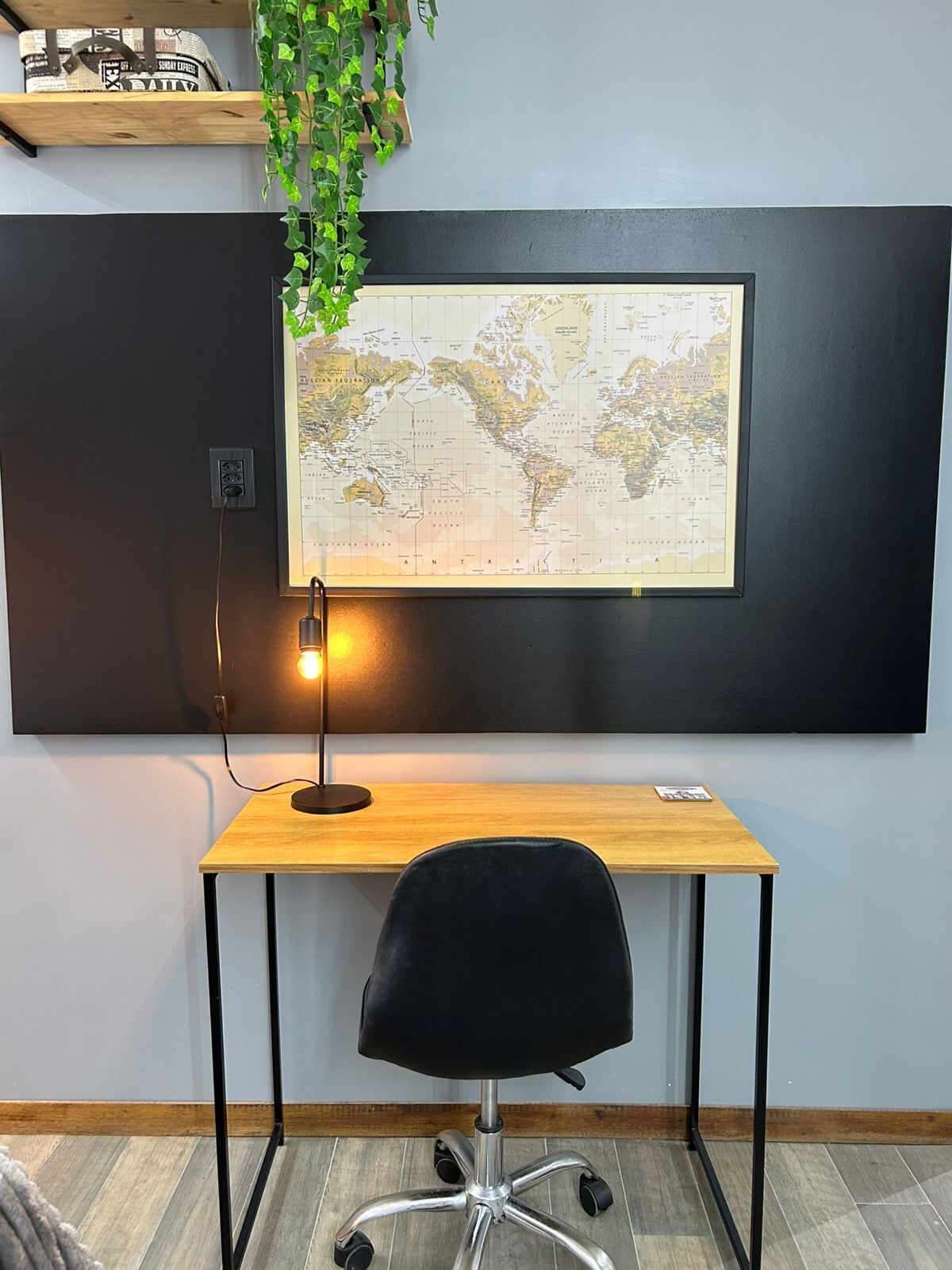 A desk with a map, a lamp, and a chair in a room with a wooden floor and a plant.