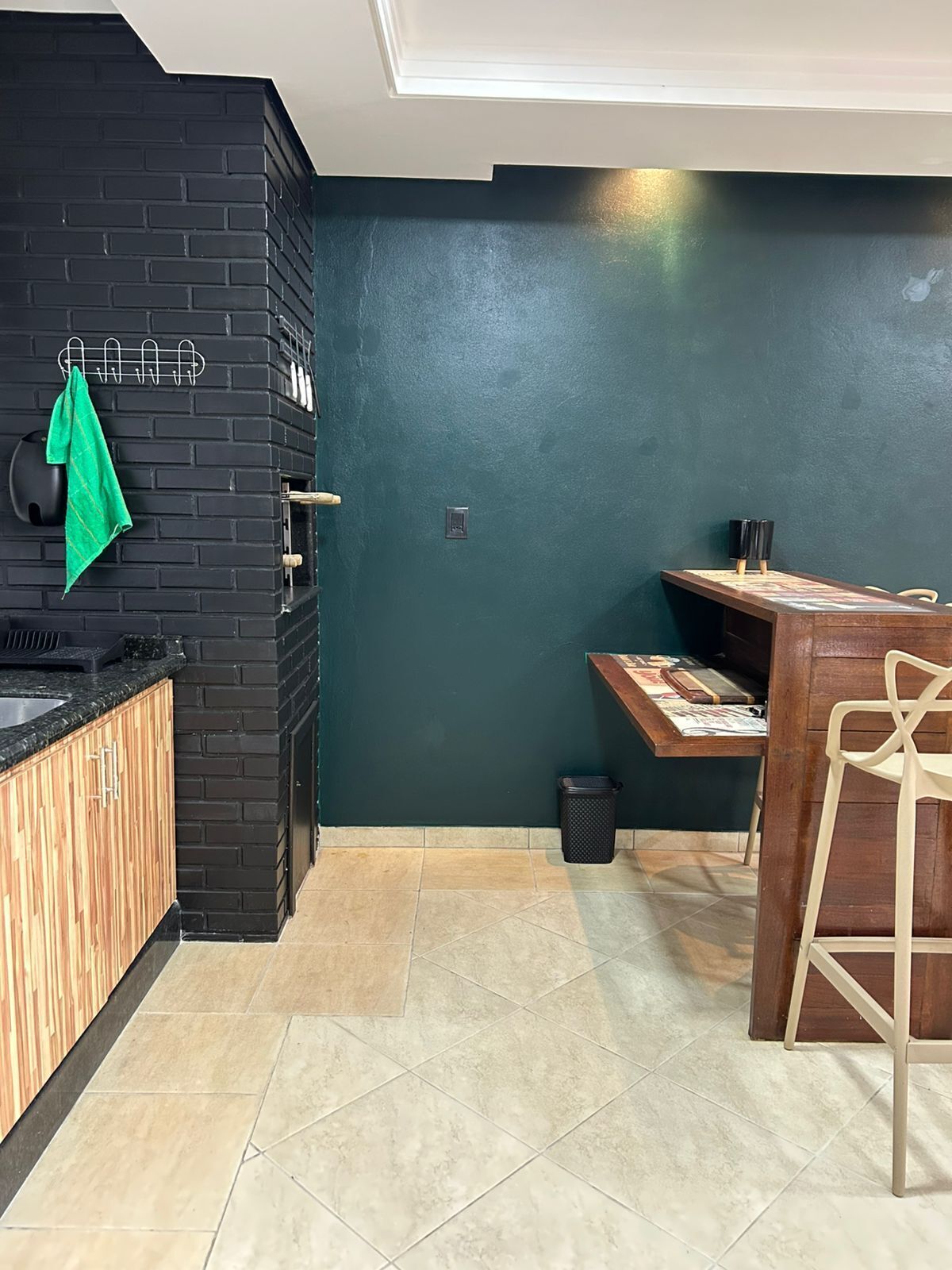 Une cuisine moderne avec un mur en briques noires, des armoires en bois, une serviette verte et une petite poubelle.