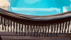 A rectangular swimming pool with a clear blue water surface, surrounded by a white fence, potted plants, and outdoor furniture.