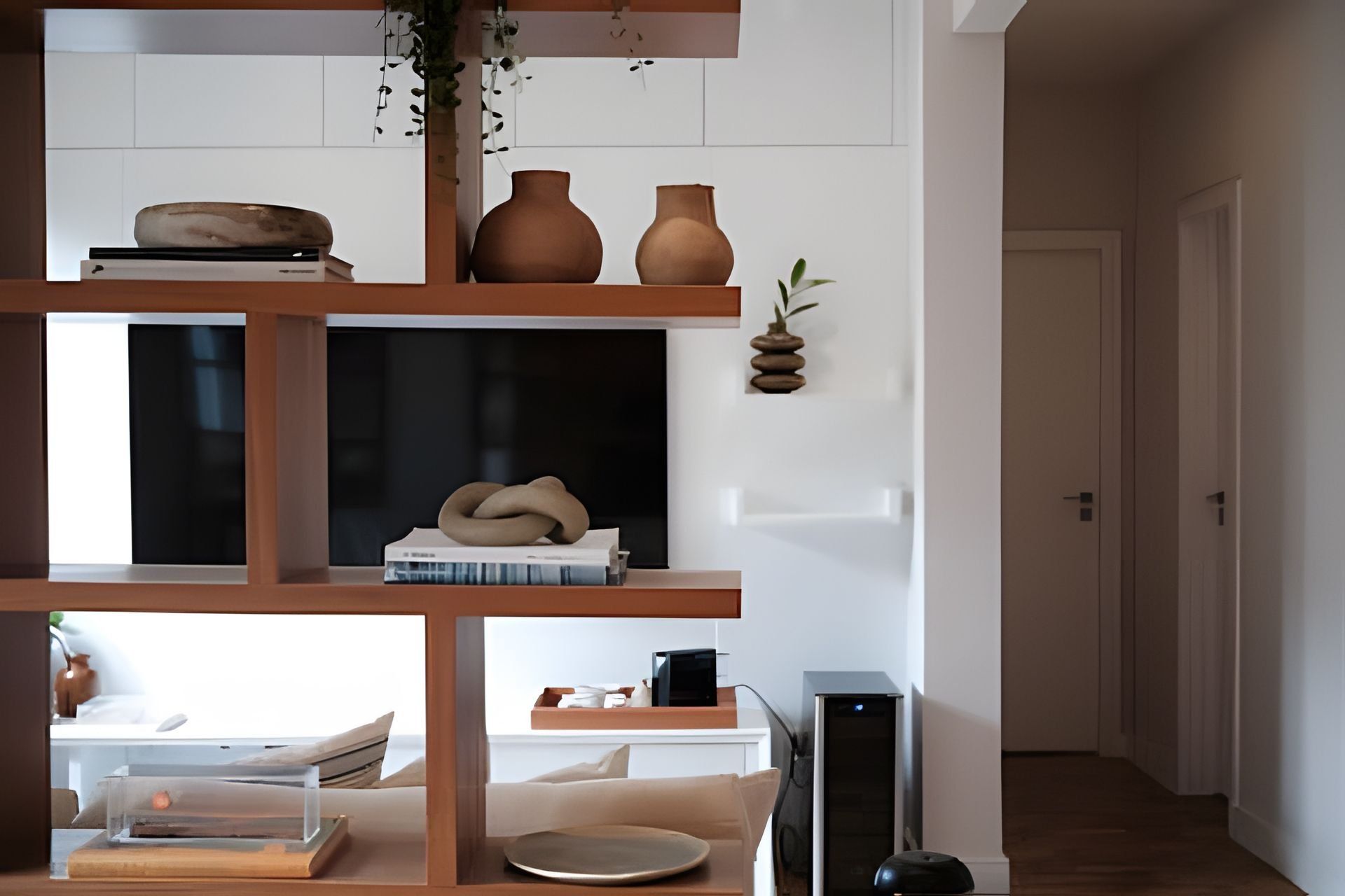 A modern living room with a wooden shelving unit displaying decorative items, a flat-screen TV, and a gaming console.