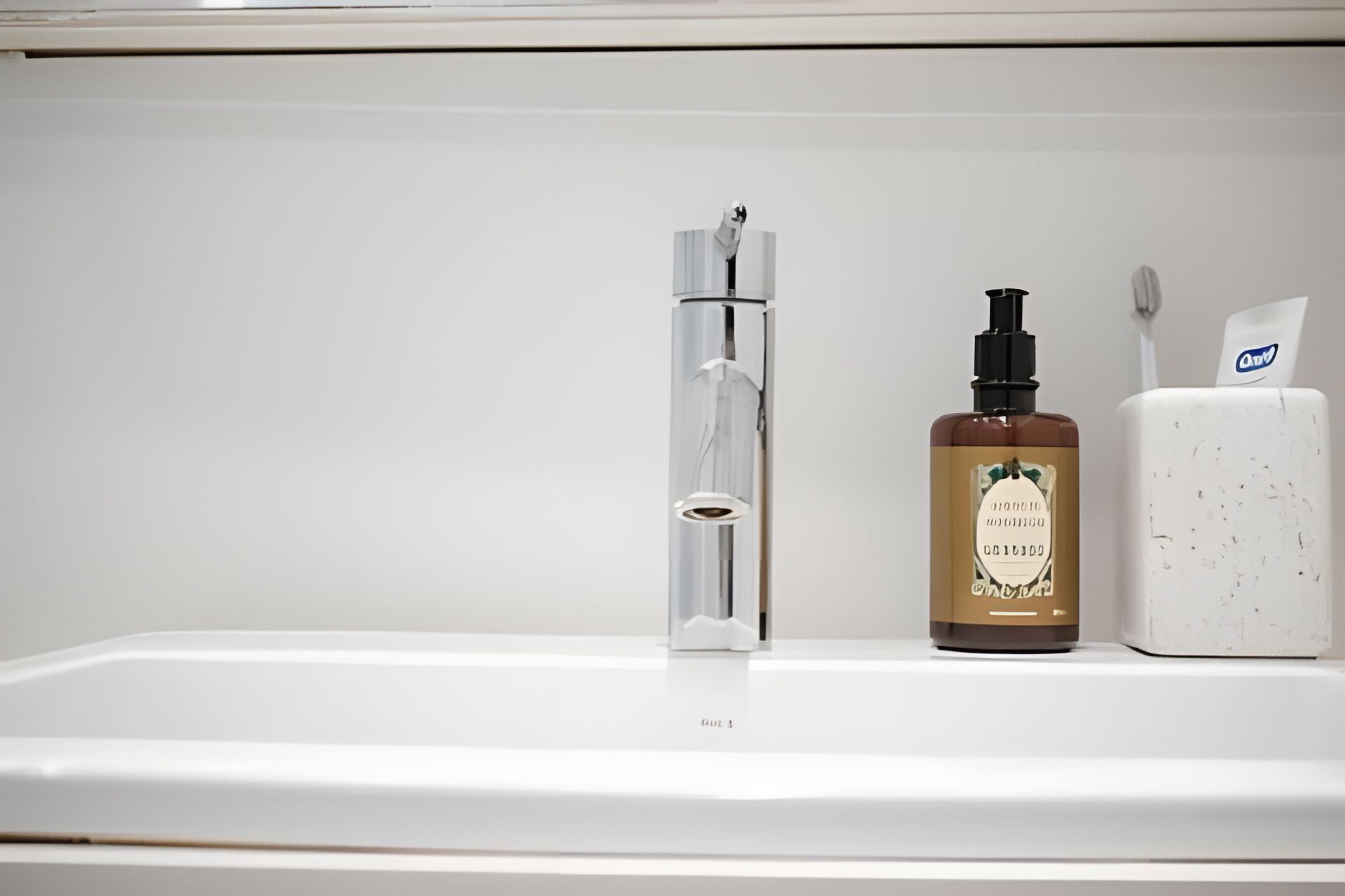 Une salle de bain avec un lavabo blanc, un robinet transparent et un flacon de savon liquide.