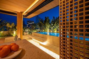 Un espace piscine extérieur moderne, avec des marches descendant vers l’eau, entouré de plantes tropicales et délimité par une clôture en bois.