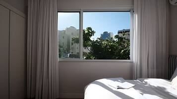 A bedroom with a large window, a bed, and a view of buildings and trees outside.