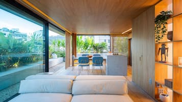 Un interior moderno con sofá, comedor y vistas al exterior con vegetación.