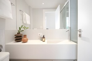 Een moderne badkamer met een witte wastafel, een spiegel, een plant en een vaas.