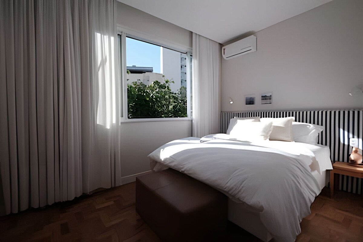 Un dormitorio moderno con una cama grande, una ventana con cortinas, una mesita de noche y un radiador.