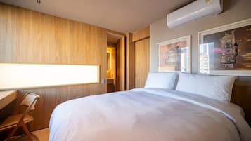 Quarto de hotel com cama, escrivaninha, cadeira e ar-condicionado fixado na parede.