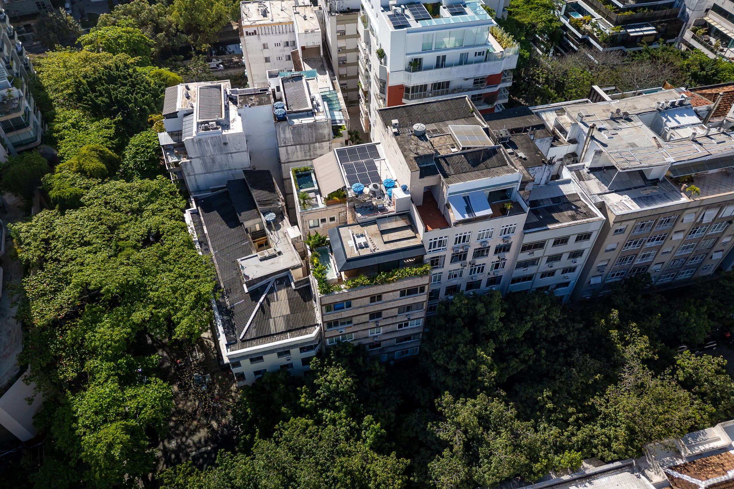 Vista aérea de uma área urbana densa com vários edifícios altos, alguns com jardins no terraço e painéis solares.