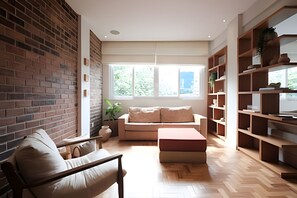 A modern living room with a brick wall, a sofa, a coffee table, and a bookshelf. - Leblon | Recém reformado, 2 quartos, 5 min da Praia – por Casapē Rio (Rio de Janeiro)