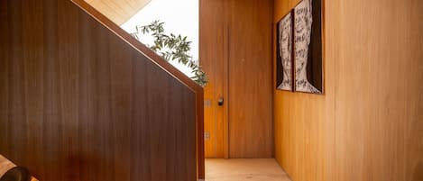 A hallway with wooden walls and a door leading to a room. There is a plant on the left and a framed artwork on the right wall.