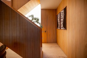Un pasillo con paredes de madera y una puerta que da a una habitación. Hay una planta a la izquierda y una obra de arte enmarcada a la derecha.