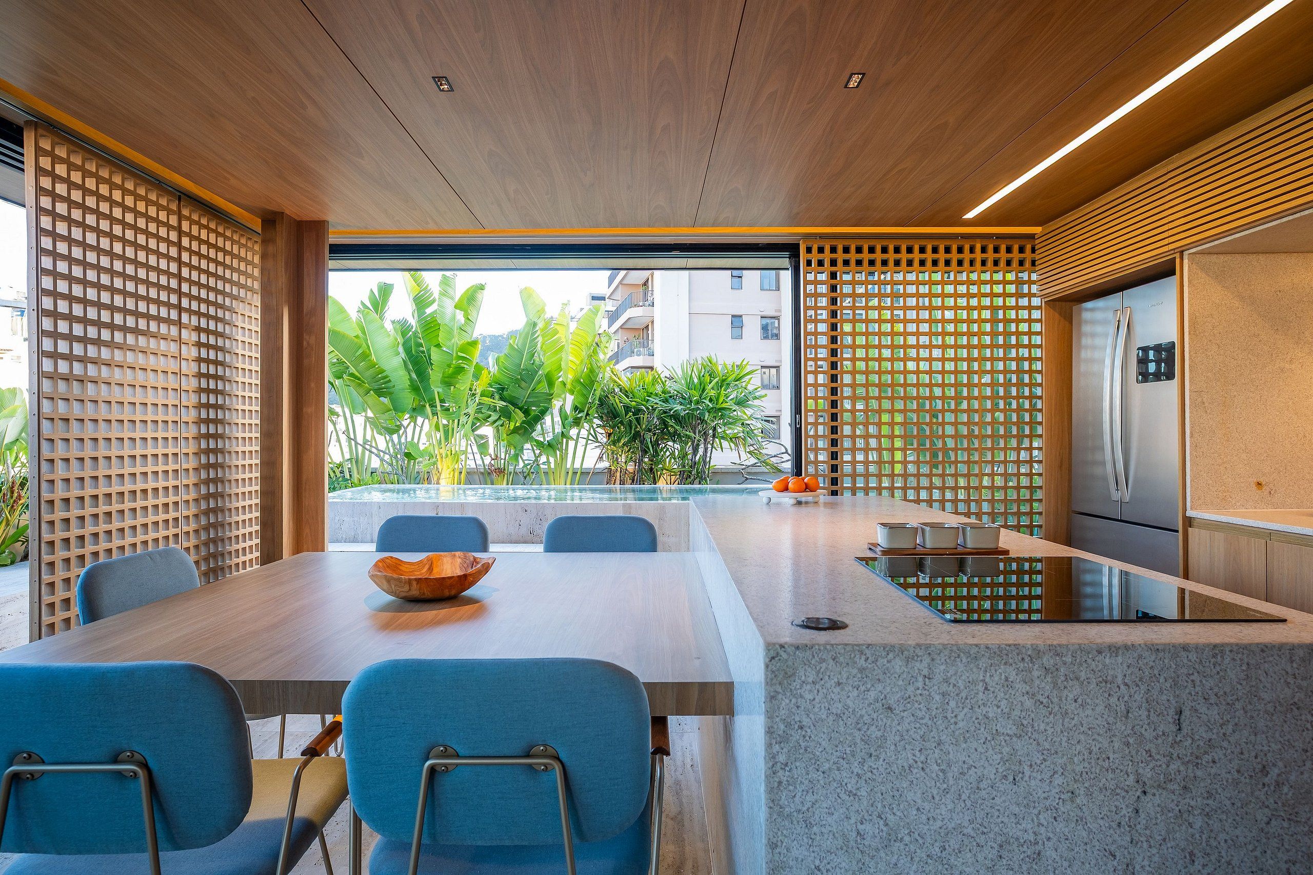 Une cuisine moderne dotée d’un réfrigérateur encastré, un coin repas avec une table et des chaises, et une vue sur une piscine et la verdure environnante.
