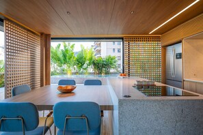 A modern kitchen with a built-in refrigerator, a dining area with a table and chairs, and a view of a pool and greenery outside. - Leblon | Recém reformado, 2 quartos, 5 min da Praia – por Casapē Rio (Rio de Janeiro)