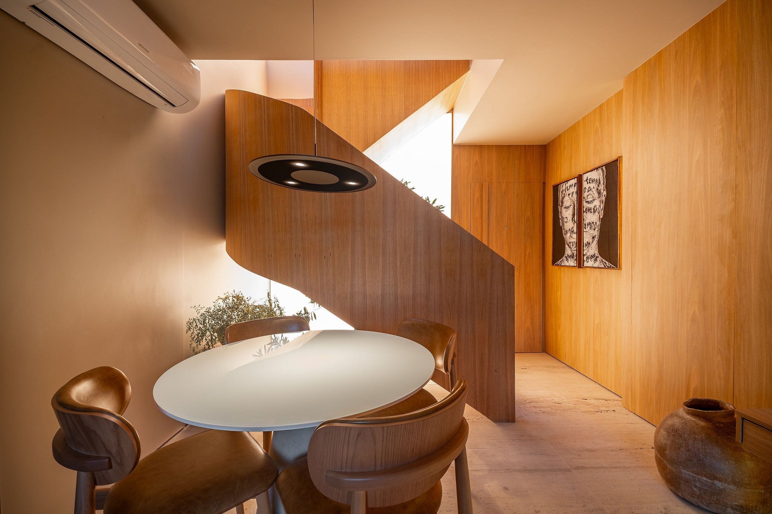 Een modern interieur met een ronde eettafel, houten stoelen, een wenteltrap en een grote vaas.