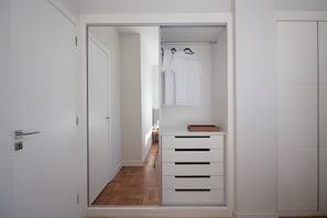 Um corredor estreito com um guarda-roupa branco, soalho de madeira e uma pequena mesa com um tabuleiro.