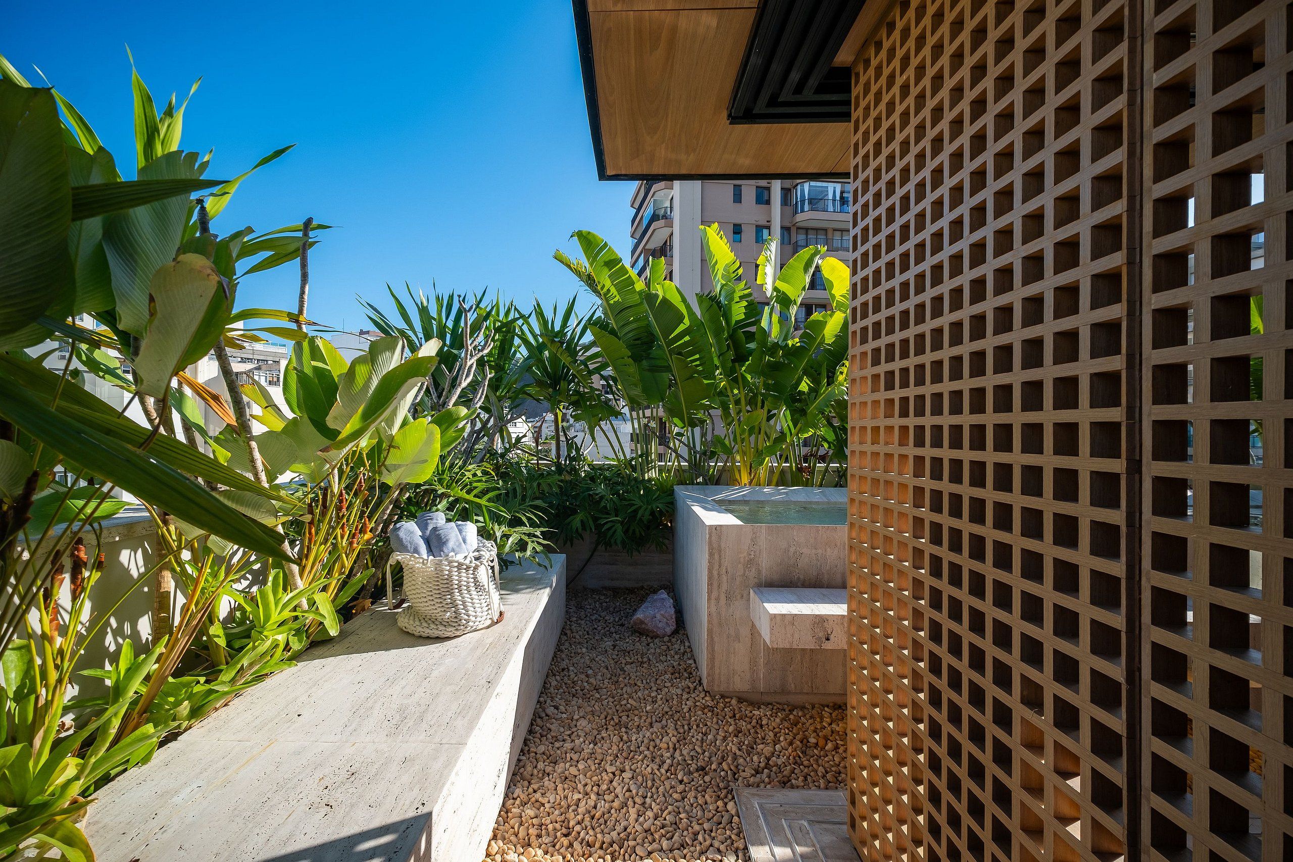 Een dakterras met diverse tropische planten, een betonnen plantenbak en een houten lattenhek.