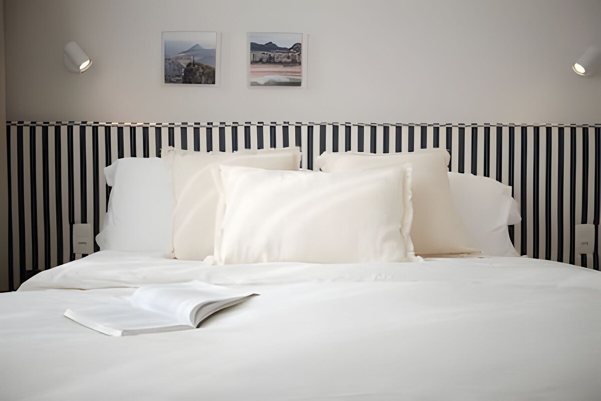 Een hotelkamer met een bed, wit beddengoed, een gestreept hoofdeinde en twee ingelijste foto's aan de muur.