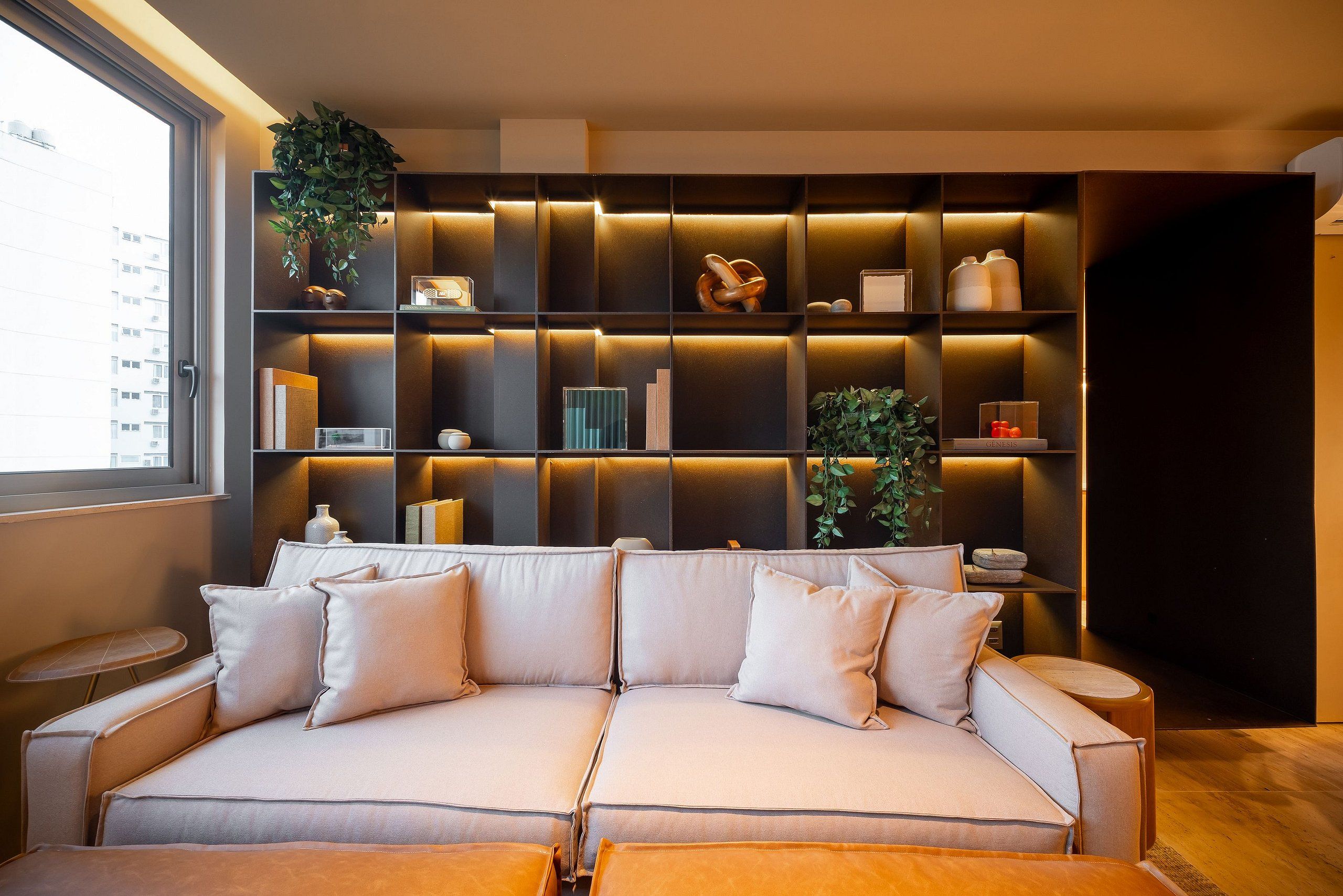 Una sala de estar moderna con un sofá, mesitas auxiliares y una estantería empotrada con diversos objetos decorativos.