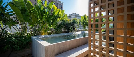Un espace piscine bordé d’une margelle en béton, entouré de verdure et agrémenté d’une structure en treillis de bois.