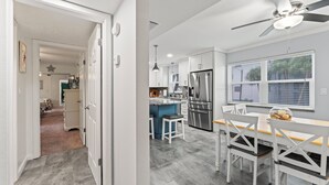 Eine moderne Küche mit weißen Schränken, einem Edelstahl-Kühlschrank und einem Essbereich mit einem Holztisch und weißen Stühlen.