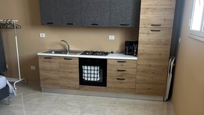 A compact kitchen with a sink, stove, and microwave. There is a dining table with a plate of sandwiches in the foreground. - Aunt Lisa home (Catania)