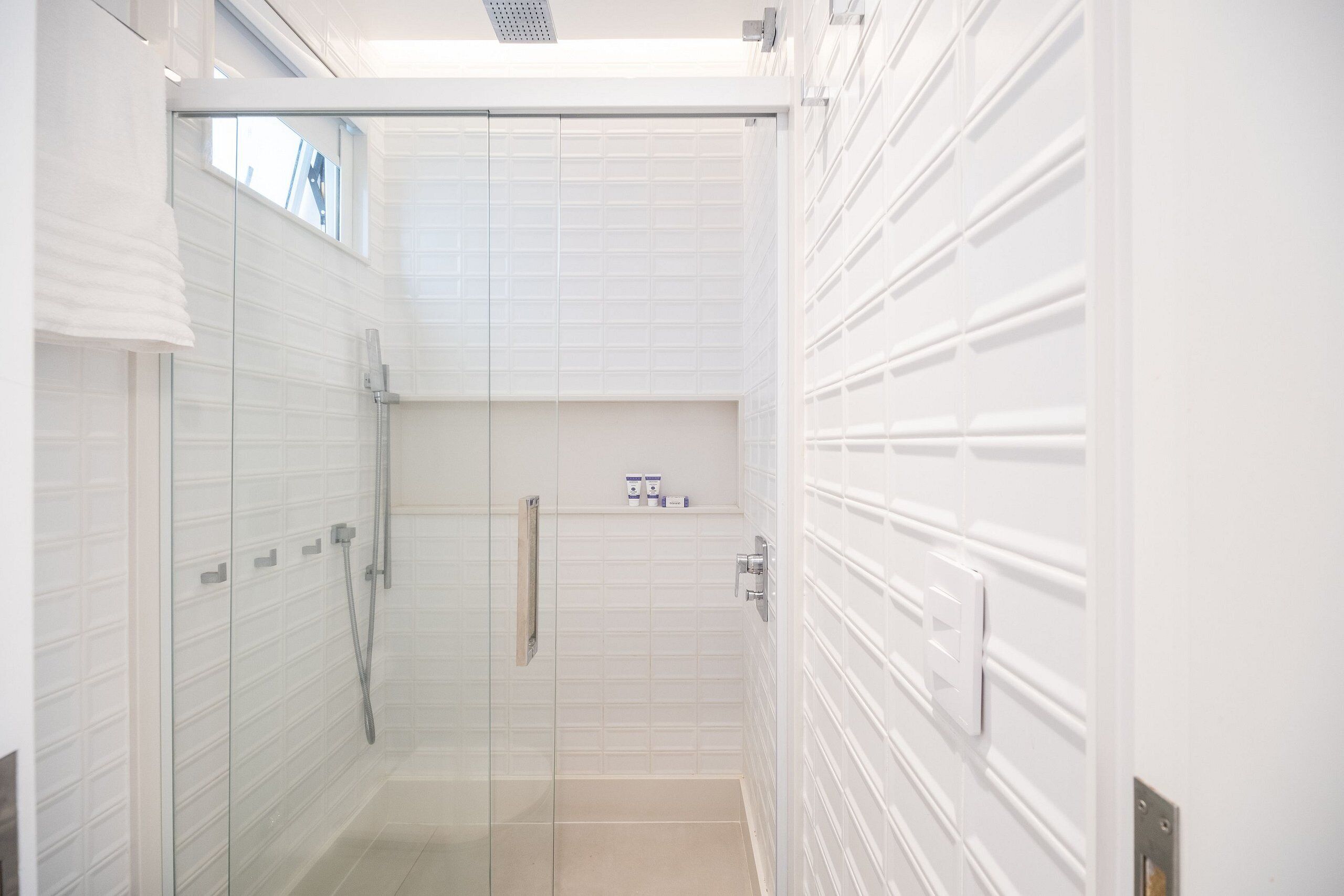 Un baño moderno con cabina de ducha de vidrio, paredes con azulejos blancos y panel de control de la ducha a la vista.
