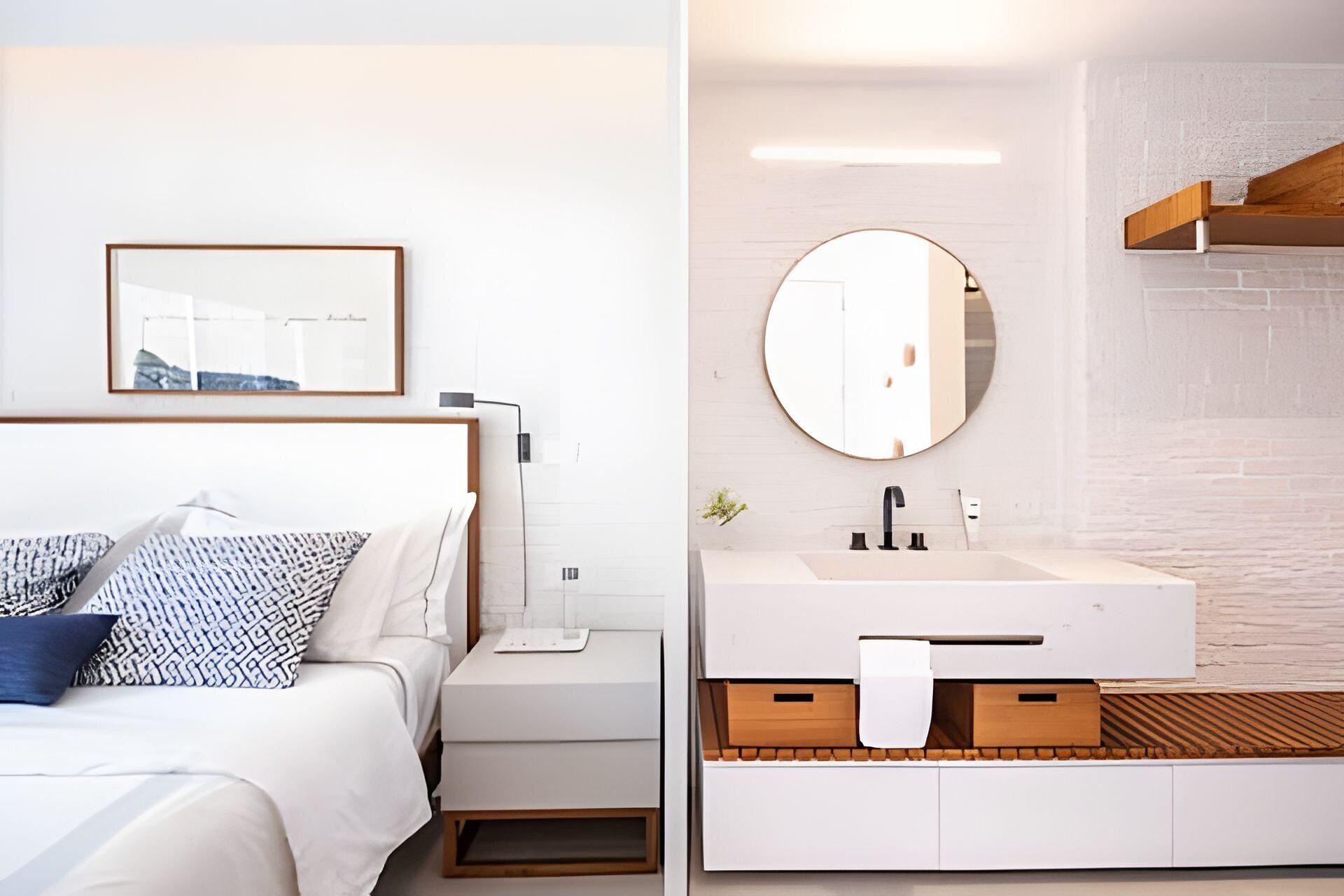 Quarto moderno com cama, mesa de cabeceira e um quadro na parede. A imagem também mostra um banheiro com pia, espelho e armários de madeira.
