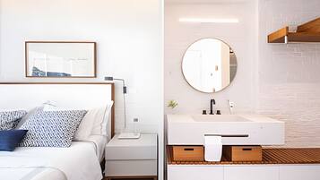 Quarto moderno com cama, mesa de cabeceira e um quadro na parede. A imagem também mostra um banheiro com pia, espelho e armários de madeira.