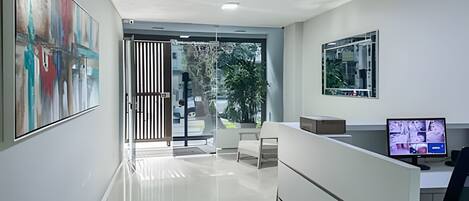 Et moderne receptionområde med en glasdør, der fører til en balkon, et skrivebord med en computer, og et stort abstrakt maleri på væggen.