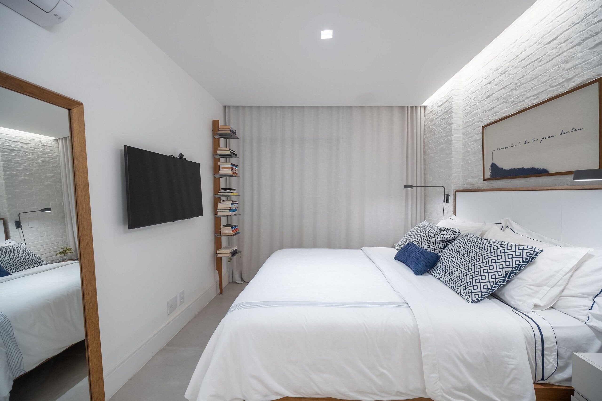 Ein modernes Schlafzimmer mit Bett, Bücherregal, Spiegel und Wand-Fernseher.